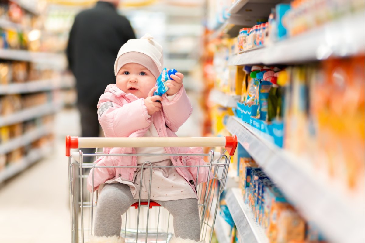 Baby in a supermarket trolley holding a food pouch. Copyright: IStock